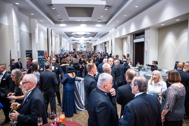 Large banquet hall filled with formally dressed people attending a gala